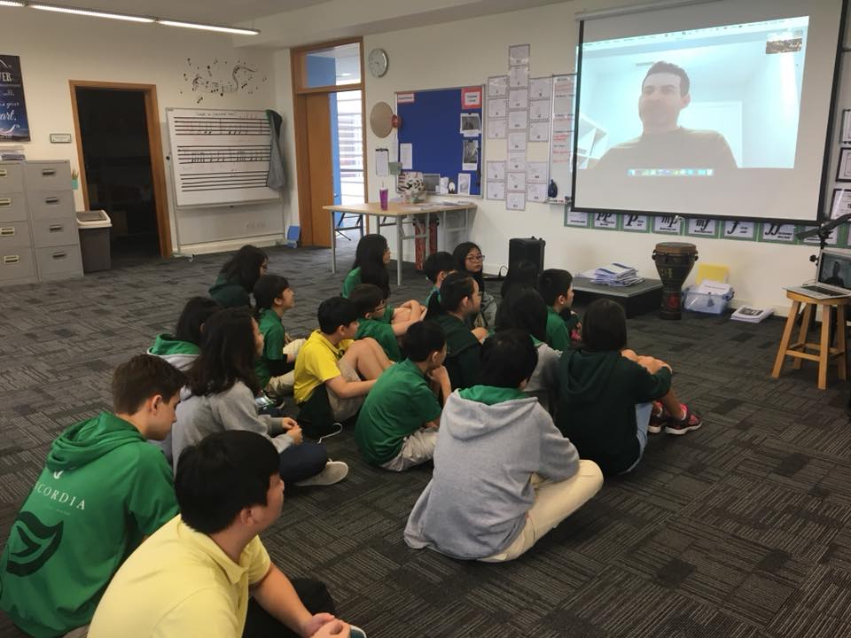 Students seated in a classroom watching Jonathan speak on a projected video call